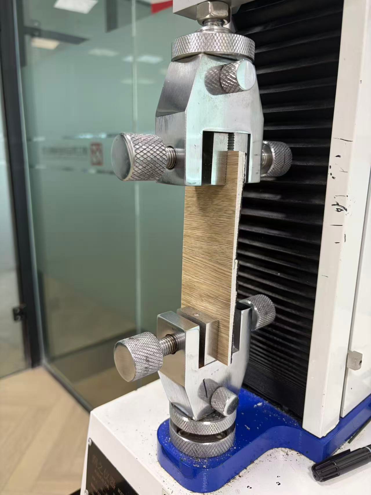 Laboratory tensile tester measuring the joint strength of a wood-look click flooring sample